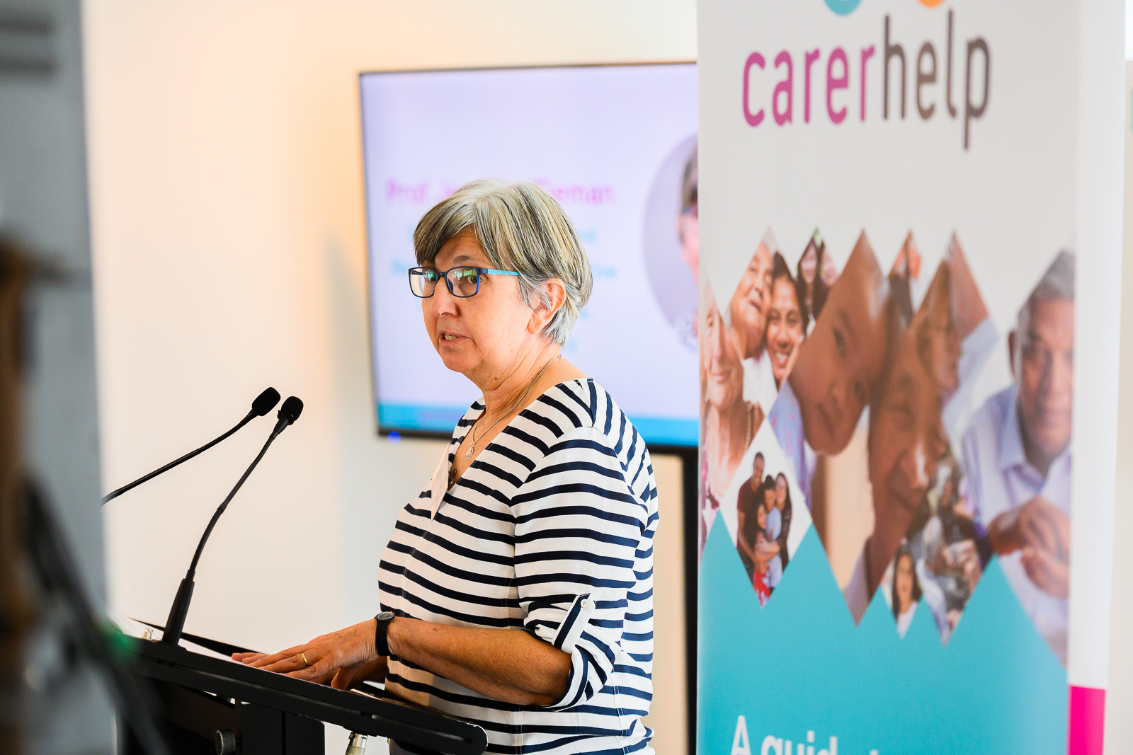 Professor Jennifer Tieman presenting the features of CarerHelp at the CarerHelp launch. She is standing at a lectern with a CarerHelp banner behind her.